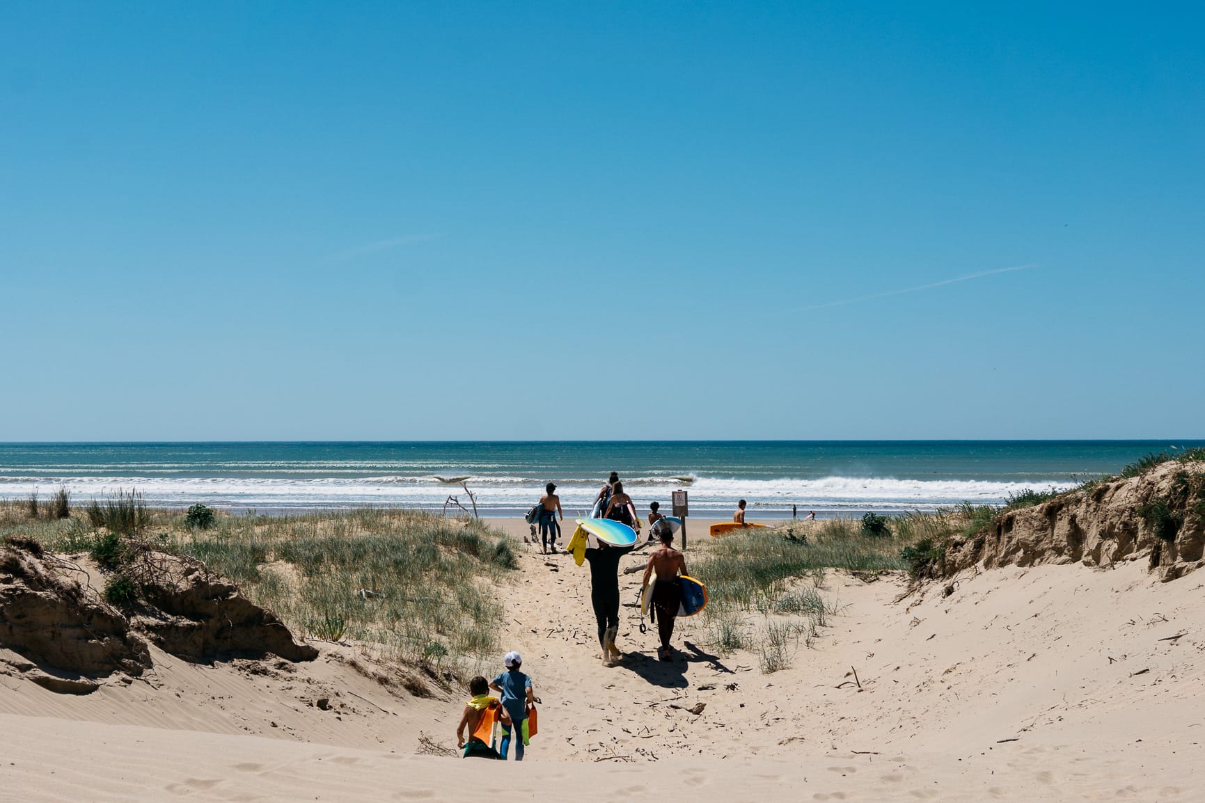 arrivee-plage-sable-planche-surf-combinaison-enfant-adulte-ado-coach-vegetation-soleil-ciel-bleu